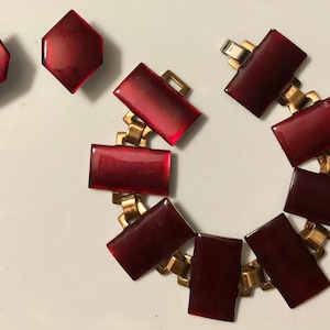Peut inclure: Un ensemble de bijoux vintage compos&eacute; d'un bracelet rouge et d'une paire de boucles d'oreilles. Le bracelet est en m&eacute;tal dor&eacute; et comporte des pierres rouges rectangulaires. Les boucles d'oreilles sont &eacute;galement en m&eacute;tal dor&eacute; et ont des pierres rouges hexagonales.