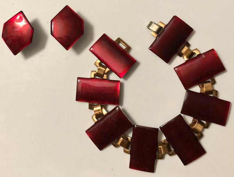 Peut inclure: Un ensemble de bijoux vintage compos&eacute; d'un bracelet rouge et d'une paire de boucles d'oreilles. Le bracelet est en m&eacute;tal dor&eacute; et comporte des pierres rouges rectangulaires. Les boucles d'oreilles sont &eacute;galement en m&eacute;tal dor&eacute; et ont des pierres rouges hexagonales.