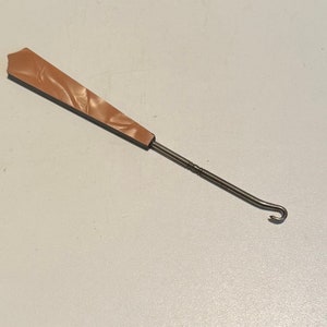 May include: A brown plastic handled crochet hook with a metal hook at the end.