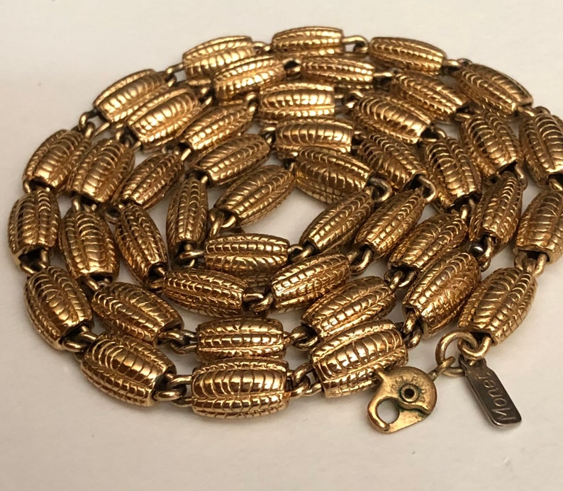 May include: A gold-tone chain necklace with a textured, ridged design. The necklace is made by the brand "Monet".