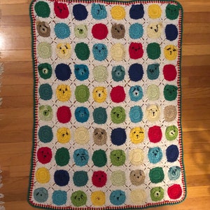 May include: A crocheted blanket with a repeating pattern of colorful circles featuring animal faces. The blanket has a white background with green, red, blue, and yellow circles.