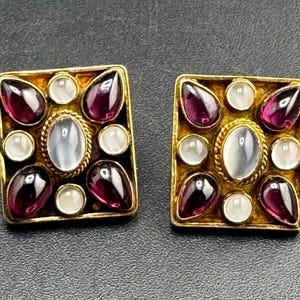 Puede incluir: Un par de pendientes cuadrados de oro con una piedra lunar ovalada central rodeada por un borde de cuerda trenzada, acentuados por cuatro cabujones de granate rojo oscuro en forma de pera y cuatro pequeñas piedras lunares blancas redondas.