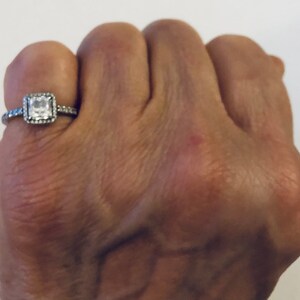 May include: A silver ring with a square-shaped clear stone surrounded by smaller stones.