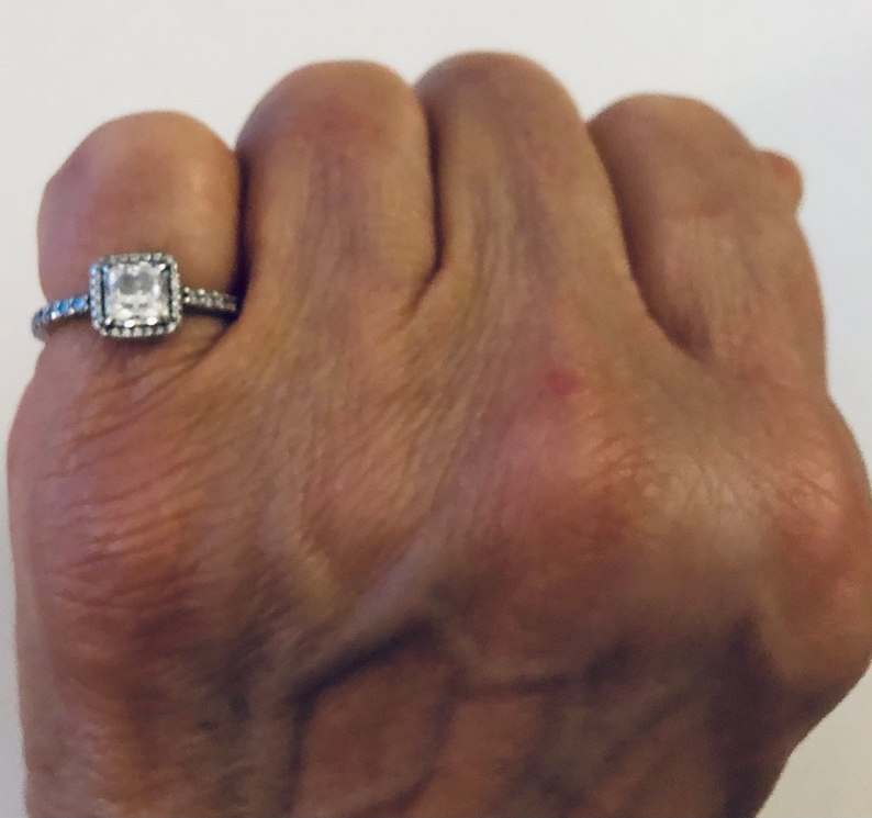 May include: A silver ring with a square-shaped clear stone surrounded by smaller stones.