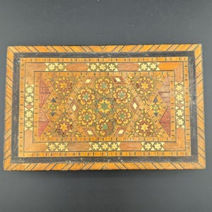 May include: A wooden box with a geometric pattern inlaid in the top. The pattern is made of different coloured woods and features stars and other shapes.