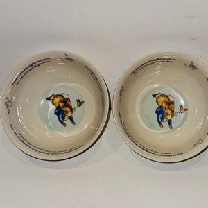 Puede incluir: Dos cuencos de cerámica blanca con un borde azul y un diseño de Peter Rabbit. Los cuencos presentan una ilustración azul y blanca de Peter Rabbit corriendo con un pájaro. El texto alrededor del borde dice "Peter Rabbit ran straight away to Mr. McGregor's garden."