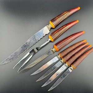 May include: Set of six vintage knives with orange and brown handles. The knives have serrated blades and a matching fork.