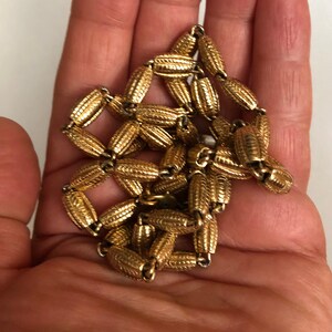 May include: A gold chain necklace with a textured, patterned design. The chain is made of small, oval-shaped links.