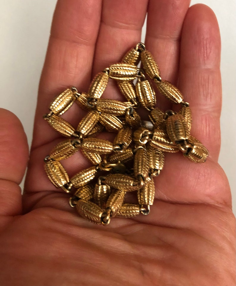 May include: A gold chain necklace with a textured, patterned design. The chain is made of small, oval-shaped links.