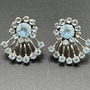 May include: A pair of silver earrings with a light blue rhinestone centre surrounded by smaller rhinestones. The rhinestones are arranged in a fan shape.