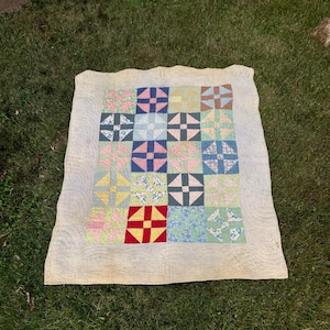 Puede incluir: Una colcha vintage con un diseño de patchwork que presenta una variedad de estampados florales en tonos de rosa, azul, verde y amarillo. La colcha está compuesta por 16 cuadrados, cada uno con un patrón diferente. La colcha está rodeada por un borde blanco.