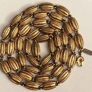 May include: A gold-toned chain necklace with a textured, oval-shaped link design. The necklace is made by the brand "Knoble".