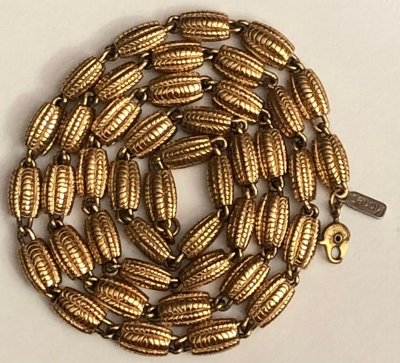 May include: A gold-toned chain necklace with a textured, oval-shaped link design. The necklace is made by the brand "Knoble".
