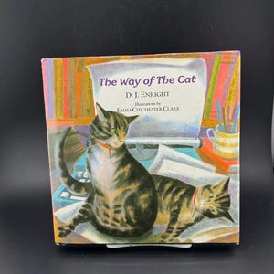 May include: A book cover for "The Way of The Cat" by D.J. Enright, illustrated by Emma Chichester Clark. The image shows two cats, a typewriter, and papers. The title is in purple text.