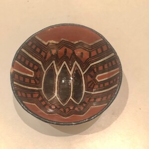 May include: A small, round ceramic bowl with a brown, black, and white geometric design. The bowl is decorated with a pattern of lines, triangles, and diamonds.
