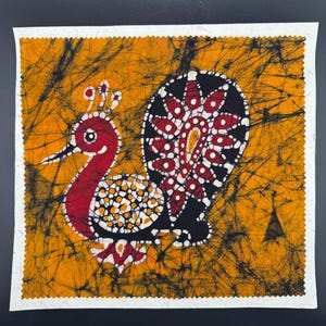 Puede incluir: Un tapiz de pared de tela batik pintado a mano que presenta un pavo real estilizado con un cuerpo rojo, plumas de cola negras y blancas y un fondo amarillo.
