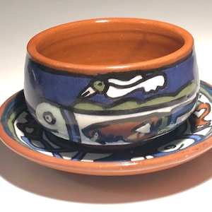 May include: A brown ceramic bowl with a blue, green, and white abstract design. The bowl is sitting on a matching saucer.