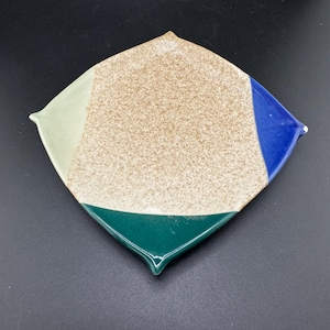 May include: A small, square ceramic dish with a speckled brown glaze. The dish has a geometric design with sections of green, blue, and light green glaze.