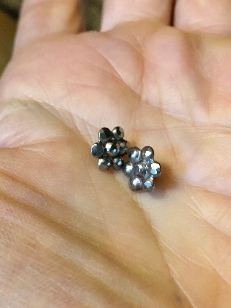 May include: Two silver flower-shaped earrings with a textured surface.