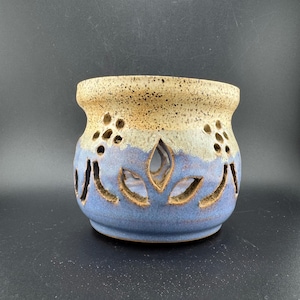 May include: A handmade ceramic candle holder in blue and tan. It has leaf-shaped cutouts and small circular openings. This decorative piece is a unique addition to any home. The holder is a decorative item.