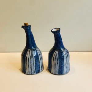 May include: Two blue and white ceramic oil and vinegar bottles with a striped design. The bottles have a cork stopper and a spout.
