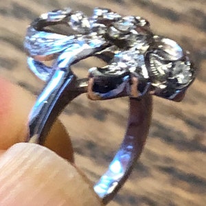 May include: A silver ring with a detailed design of a stylized flower. The ring is open and has a smooth band.