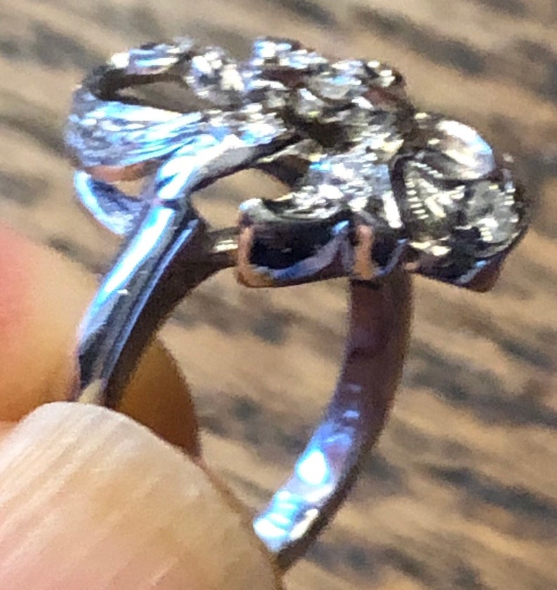 May include: A silver ring with a detailed design of a stylized flower. The ring is open and has a smooth band.