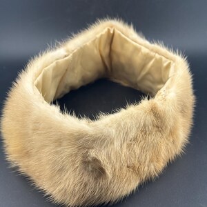 May include: A light brown fur collar with a soft, beige interior lining. The collar is circular and appears to be made of a soft, plush material. The fur has a natural, textured appearance, and the collar is set against a dark background.