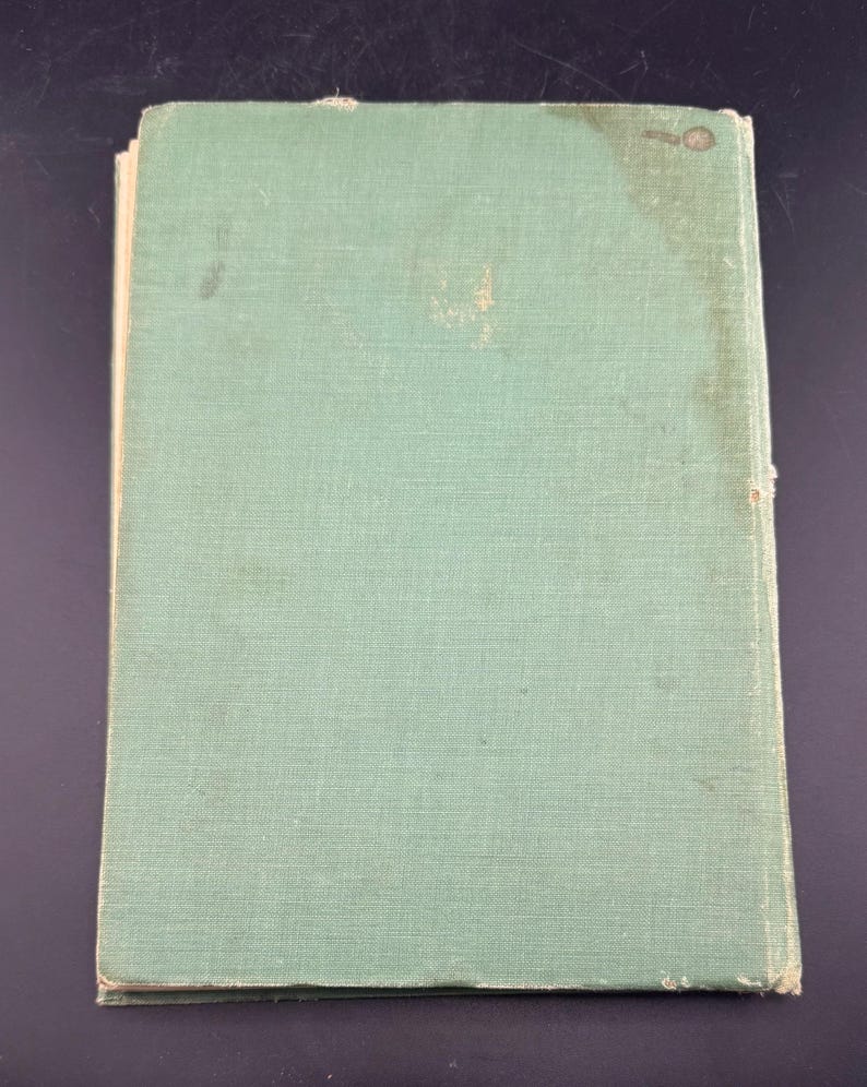 May include: A vintage book with a faded, pale green cover. The cover has a textured appearance and shows signs of wear, including discoloration and small spots. The book's edges are slightly worn, suggesting age and use. The overall aesthetic is one of a well-loved, antique item.