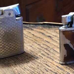 May include: Two vintage lighters, one silver with a textured design and one brown with a silver design.