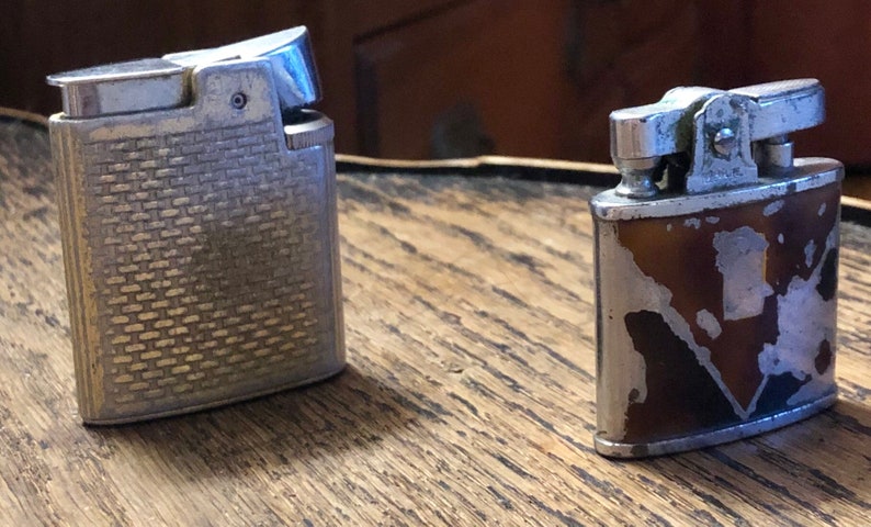 May include: Two vintage lighters, one silver with a textured design and one brown with a silver design.