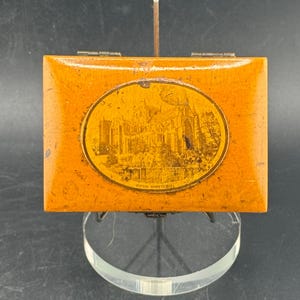 May include: A rectangular, wooden box with a hinged lid. The box is a warm orange color with a slightly distressed finish. An oval image of a building is on the lid. The text "RIPON MINSTER" is below the image.