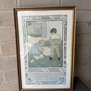 Puede incluir: Impresión vintage enmarcada con un marco dorado. La obra de arte representa a dos niños jugando con bloques en una habitación. La impresión incluye texto en la parte superior e inferior y está rodeada por un borde floral.
