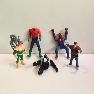 May include: A set of five action figures featuring characters from the Spider-Man universe. The figures include Spider-Man, Venom, Doc Ock, Green Goblin, and a human figure. The figures are made of plastic and are painted in various colors.