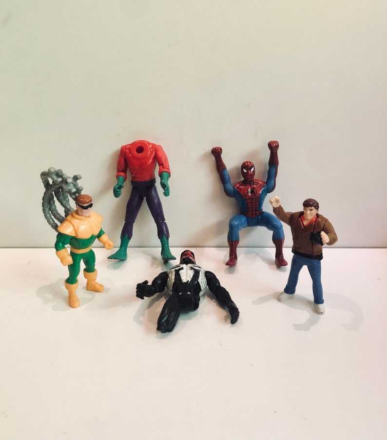 May include: A set of five action figures featuring characters from the Spider-Man universe. The figures include Spider-Man, Venom, Doc Ock, Green Goblin, and a human figure. The figures are made of plastic and are painted in various colors.