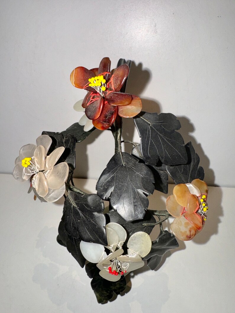 May include: A decorative floral sculpture featuring dark gray leaves and flowers in shades of brown, white, and yellow. The flowers have intricate details with yellow and red accents, creating a naturalistic aesthetic. The sculpture is likely made of stone or a similar material.