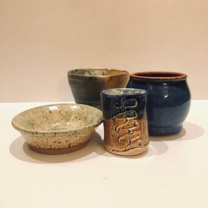 May include: Four handmade ceramic pieces in various shades of blue, green, and brown. The pieces include a small bowl, a larger bowl, a small cup, and a larger cup.