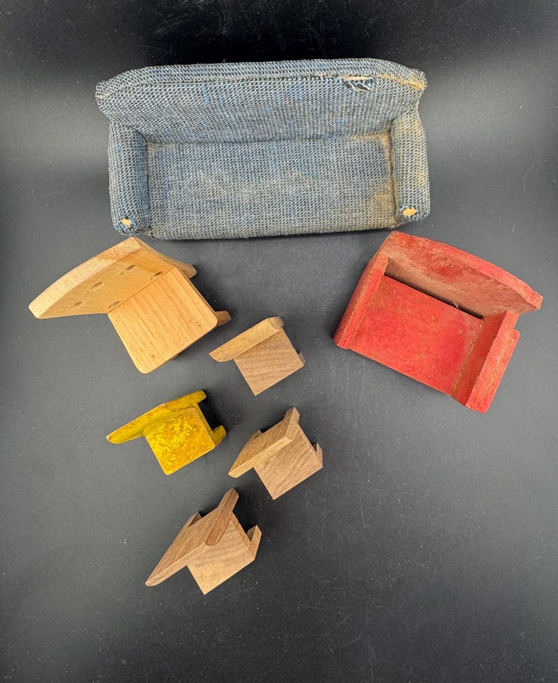 May include: A miniature blue fabric sofa with a rectangular shape and several wooden toy pieces in various colors. The wooden pieces include a natural wood color, yellow, and red.