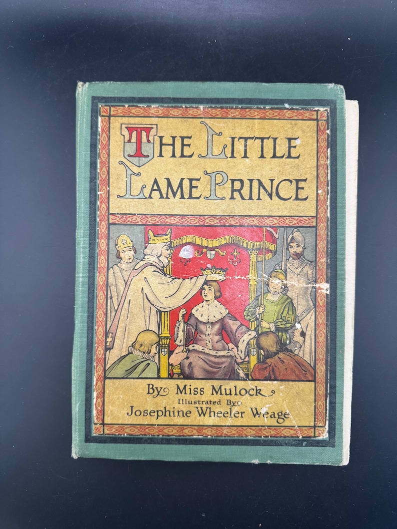 May include: A vintage copy of "The Little Lame Prince" book. The cover features a green border and a detailed illustration of a coronation. The title is displayed in ornate lettering, with the author's and illustrator's names below the illustration.