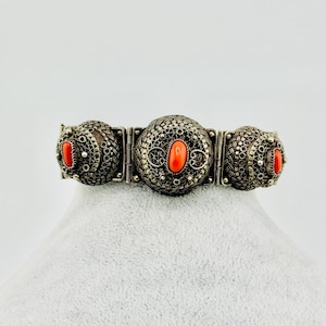 May include: A silver bracelet with three round filigree charms, each set with a red coral stone. The bracelet is made of interlocking links.