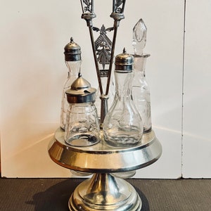 May include: A silver and glass condiment set with a decorative stand. The set includes four glass bottles with silver tops and a silver pouring spout.