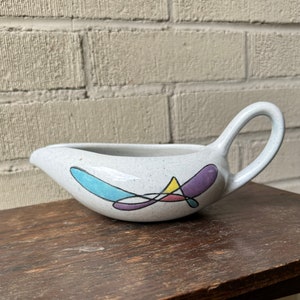 May include: A white ceramic gravy boat with a speckled glaze and a colorful abstract design in blue, purple, yellow, and pink.