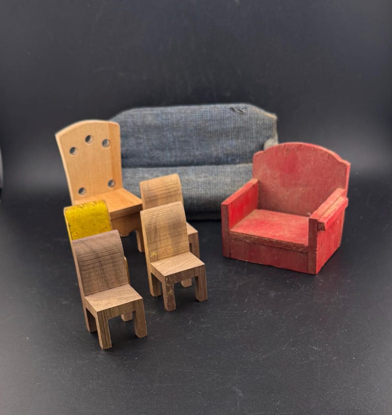 May include: A collection of miniature wooden furniture, including chairs and a small red armchair. The chairs vary in design and wood tone, with one featuring a yellow seat cushion. A small, blue fabric sofa is in the background.