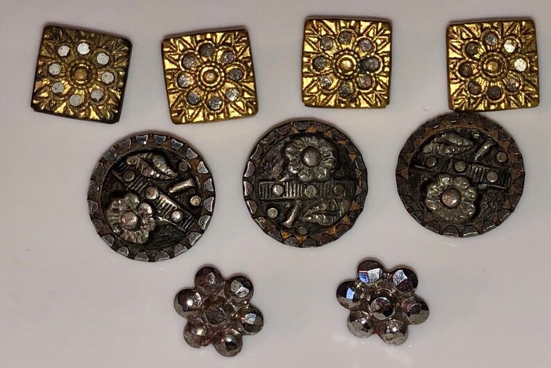 May include: Assortment of vintage buttons in gold and silver tones. Some buttons feature a floral design, while others have a geometric pattern.