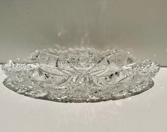 May include: A clear glass serving bowl with a cut glass design. The bowl is oval shaped and has a scalloped edge.