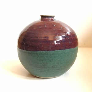 May include: A round ceramic vase with a dark brown glaze on the top half and a green glaze on the bottom half.