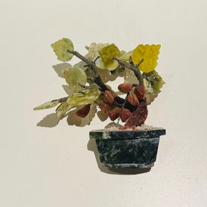 May include: A jade bonsai tree with green, yellow, and red leaves, in a dark green stone pot. The tree is made of polished jade stones and is a decorative object.