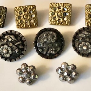 May include: Assortment of vintage buttons in gold and silver tones. The buttons feature various designs, including floral motifs, geometric patterns, and a raised design.
