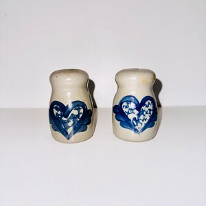 May include: A pair of salt and pepper shakers made from ceramic. The shakers are white with a blue heart design. The hearts are outlined in blue and have a white and blue speckled pattern inside.