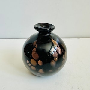 May include: A small, round black glass vase with a glossy finish and scattered gold flecks.